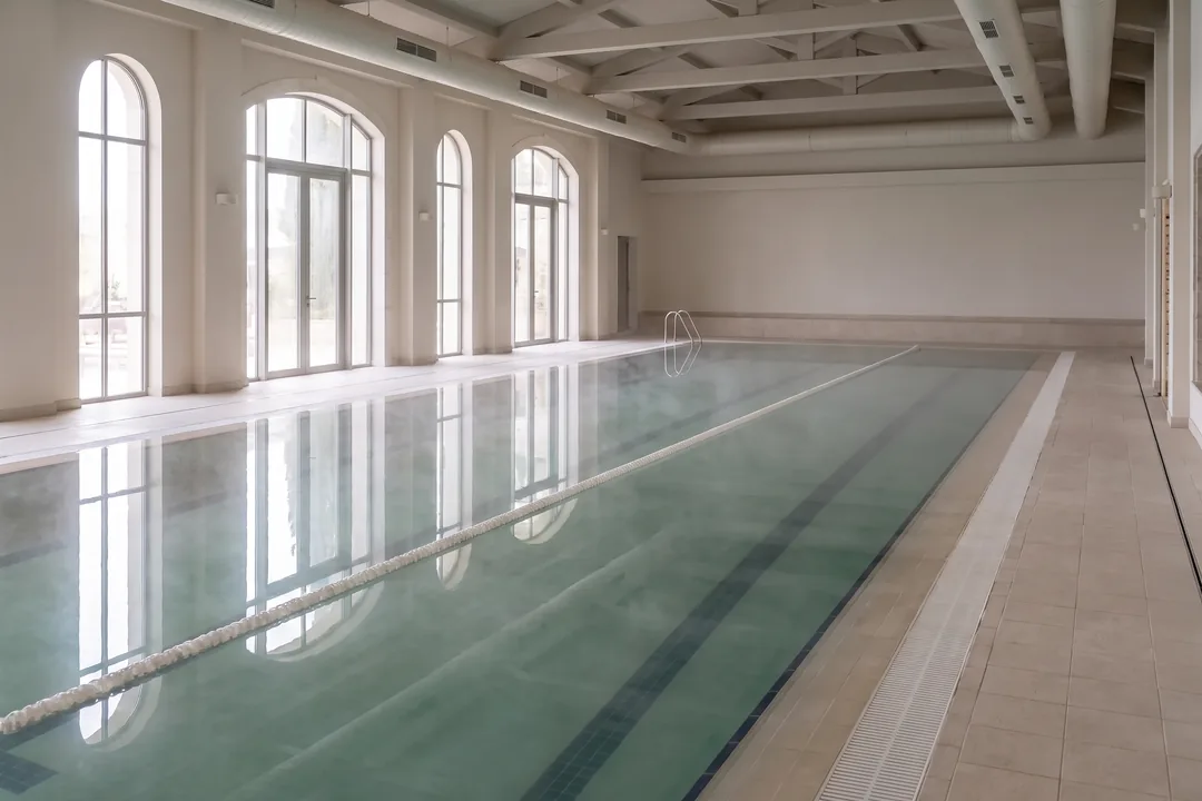 An indoor hotel lap pool closed for maintenance, its water hazy and grey-green so the floor lines barely show.